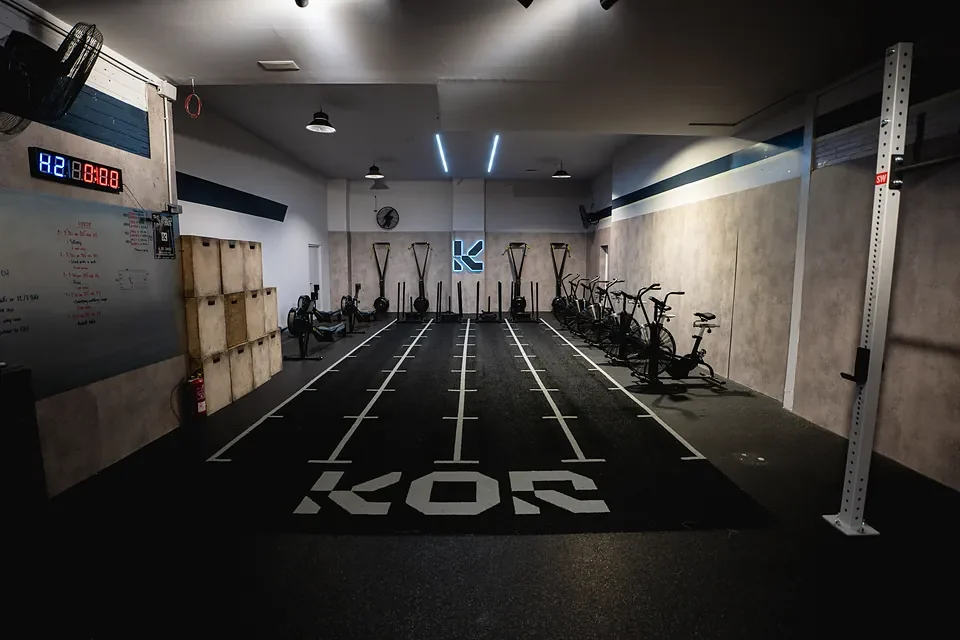 Pista de Hyrox de KOR Training Club, con trineos, bicicletas y el logo de KOR pintado en el suelo